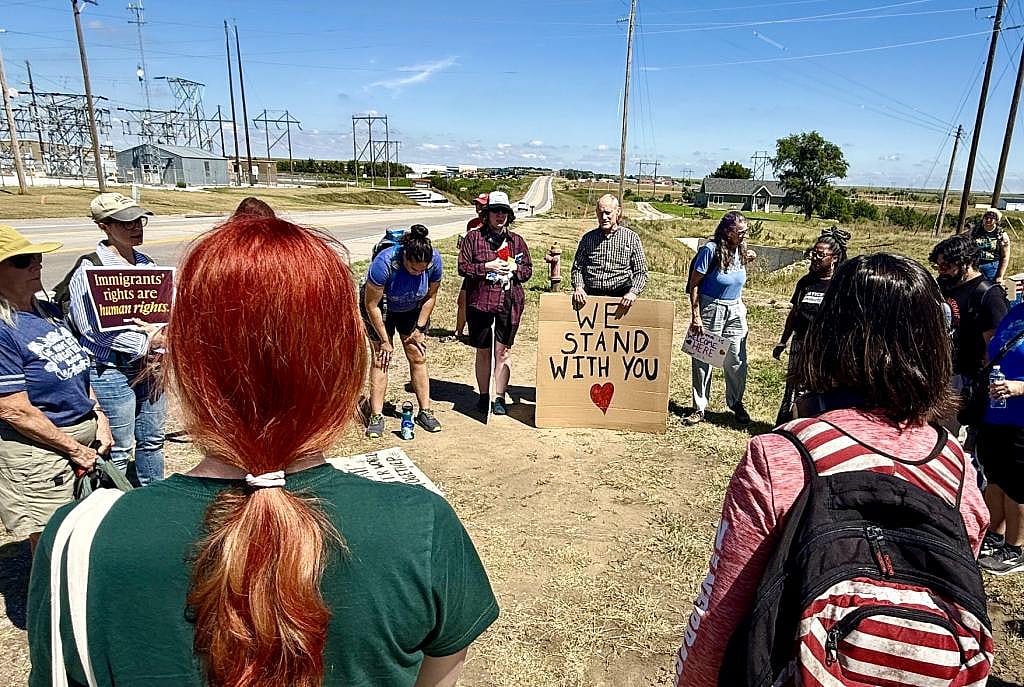 A group traveling from Lincoln to the McCook rally stands in a circle to pray, with some holding signs of support for immigrants. The McCook immigration detention facility is  down the highway about a quarter of a mile.