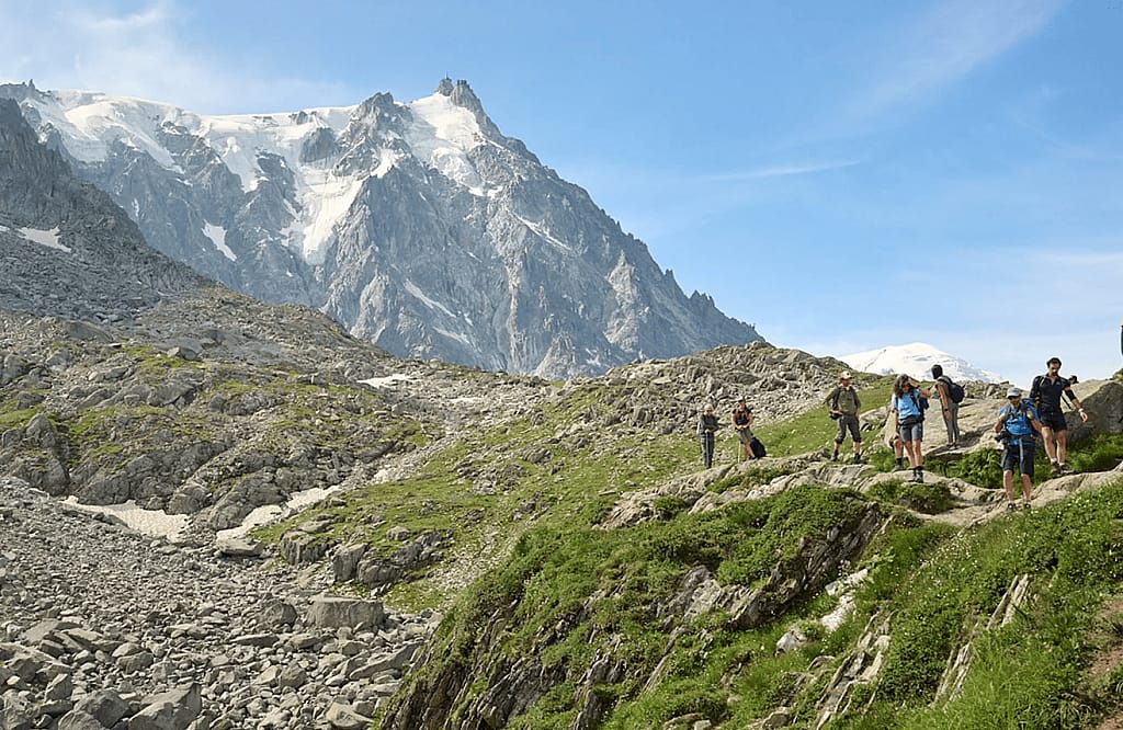 A group of 7 people hiking in the alps with snow visible on the peak in the background.