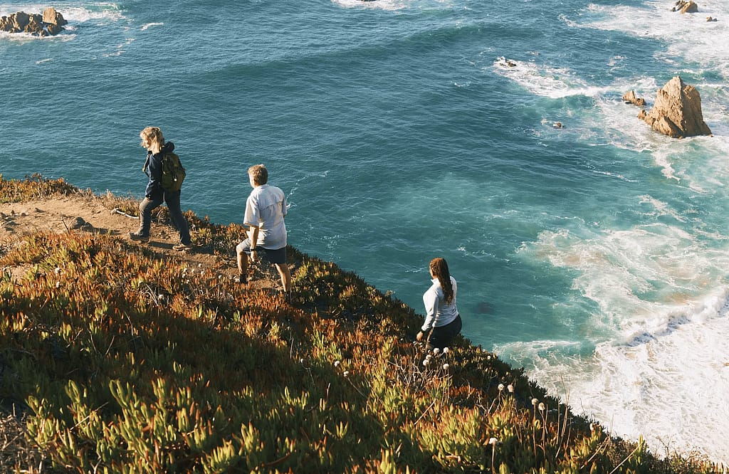 Three people hiking on a trail near the ocean on the Camino de Santiago.