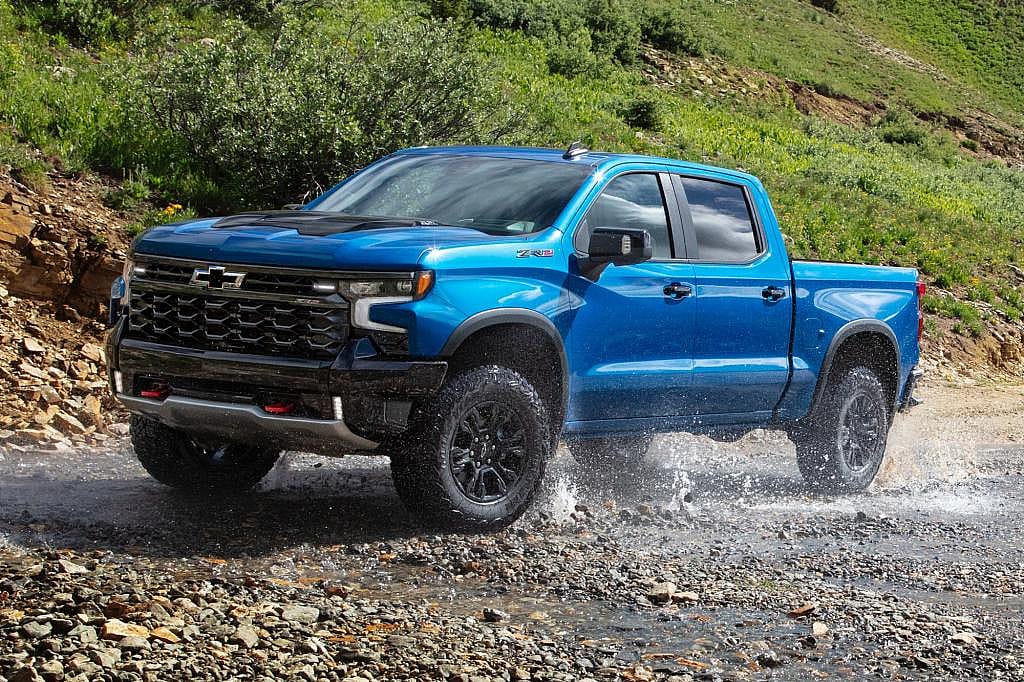 2026 Chevrolet Silverado 1500 ZR2 in Riptide Blue driving on a wet, rocky trail, front-quarter view.