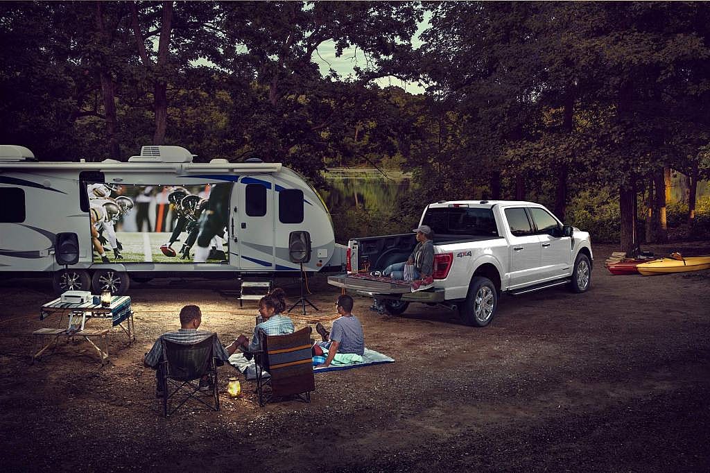 A 2024 Ford F-150 powers an entire campsite with its Pro Power Onboard feature, with people gathered to watch a football game.