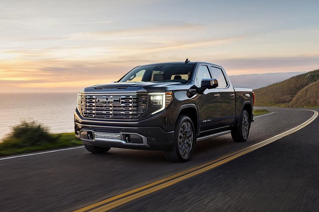 2026 GMC Sierra 1500 Denali Ultimate in Onyx Black, driving on a coastal highway at sunset.