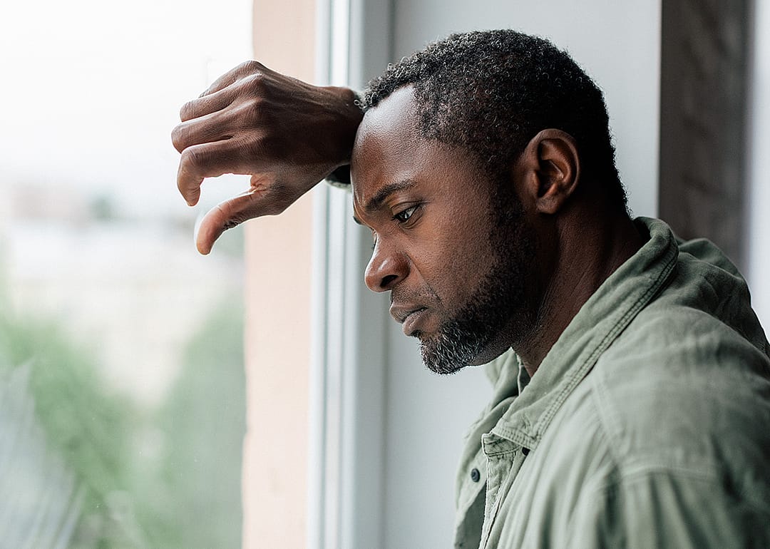 A sad-looking man with graying hair looking out window.