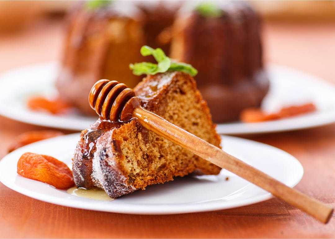 A slice of honey cake on a plate with a honey dripper.