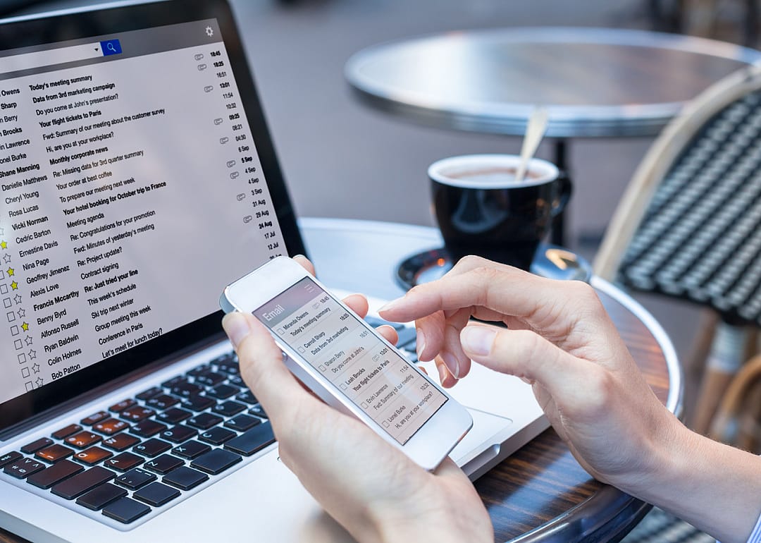 Person reading email on phone with laptop computer.