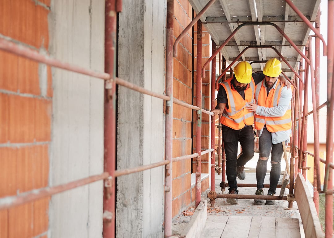 Construction worker helping injured coworker at job site.