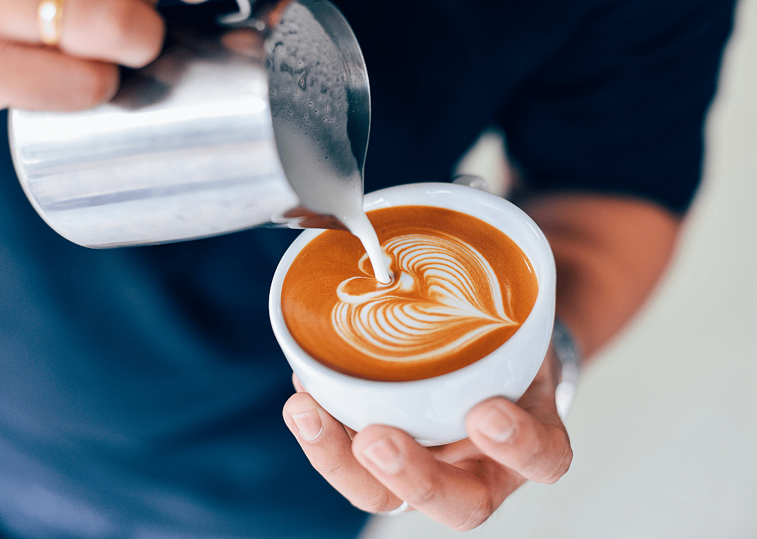 Barista pouring milk in coffee drink.