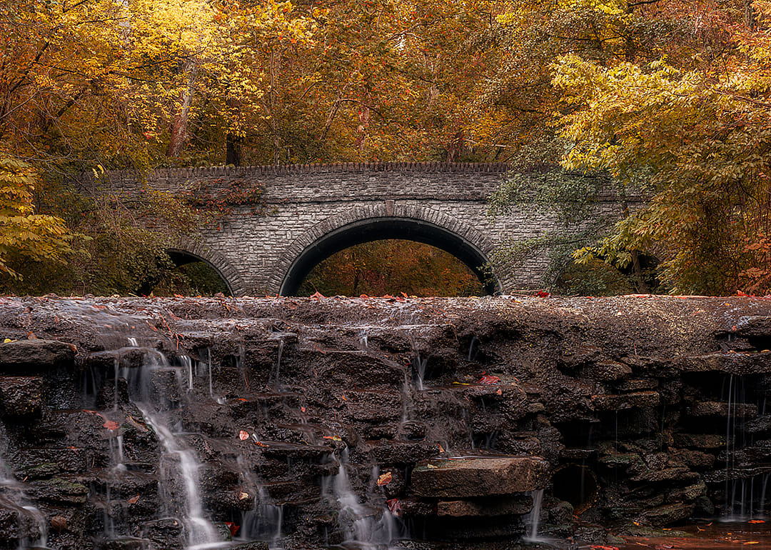 A waterfall near a stone arched bridge in Sharon Woods Park