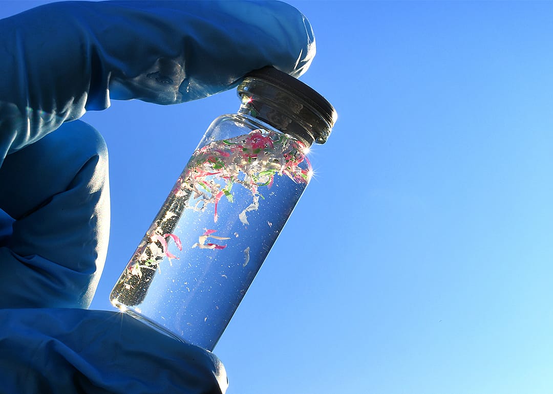 Glass vial with water samples contaminated with microplastics against blue sky.