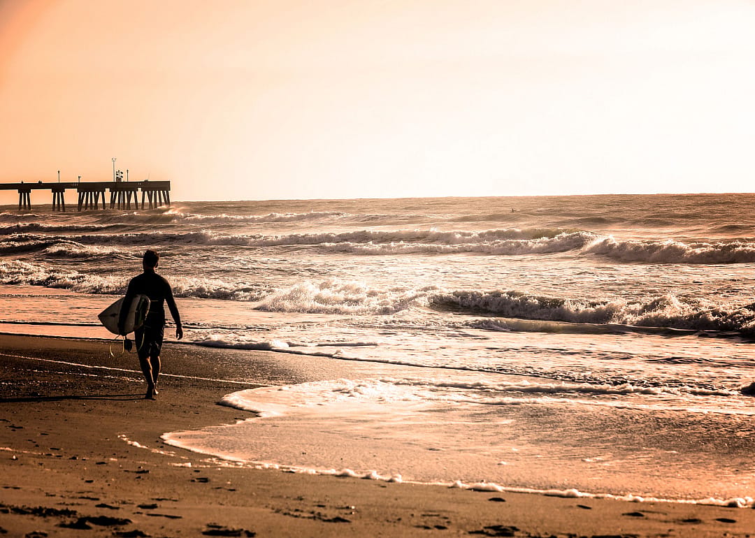 Man with surfboard on beach with sunset.