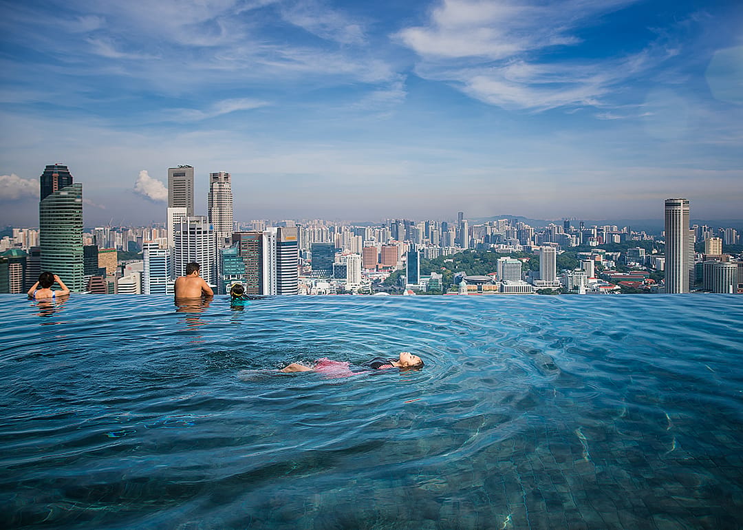 People swimming in Singapore rooftop infinity pool, looking out toward the city.
