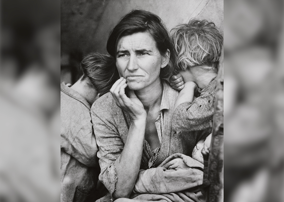 A woman with her hand to her face holding an infant with young two children facing away from the camera.