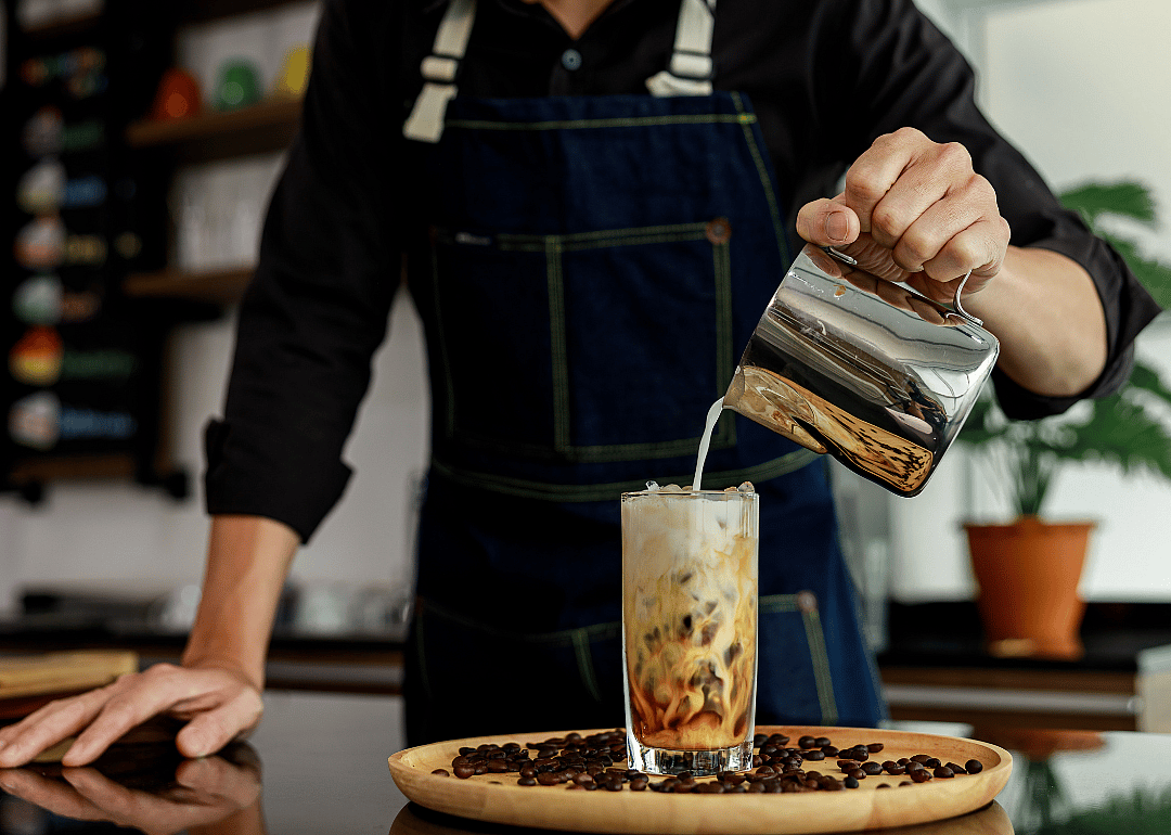 Barista pouring milk in coffee drink.