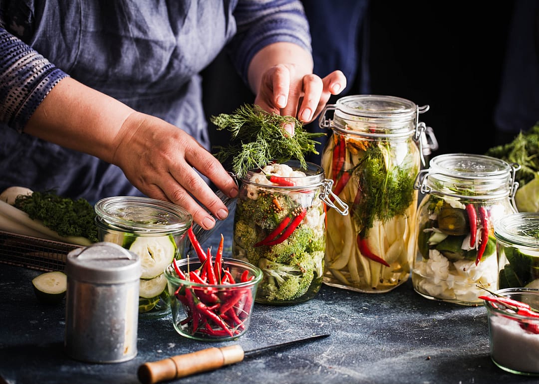 Person preparing pickled vegetables in jars.