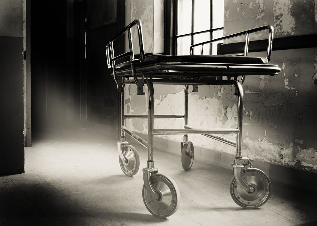 Black and white image of hospital gurney in an old room.