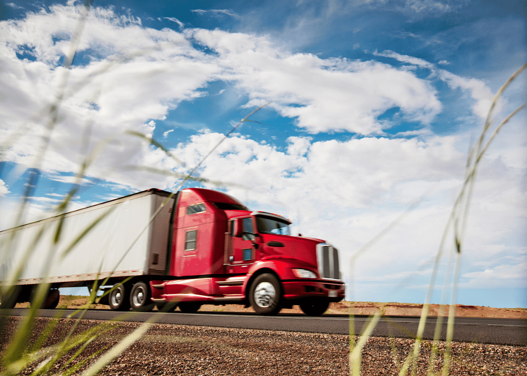 A red semi truck speeds along a highway
