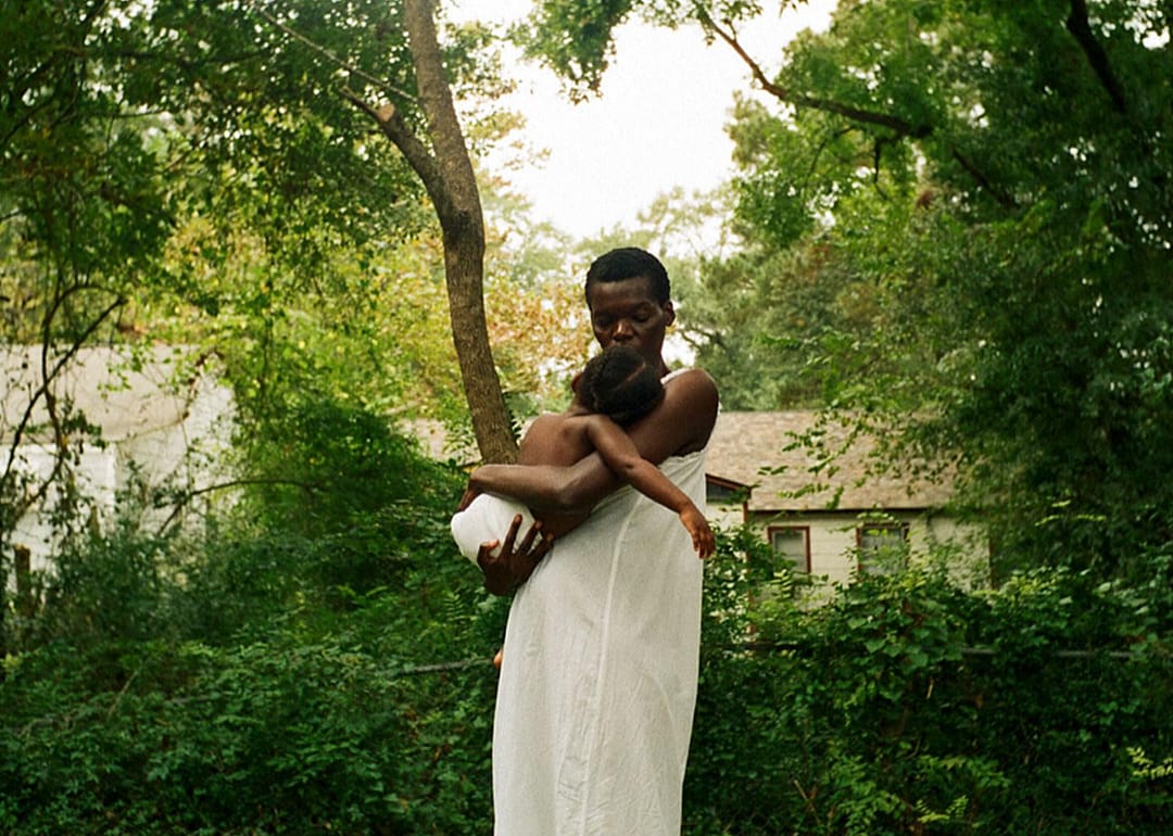 Woman holding child in an image from ‘All Dirt Roads Taste of Salt’.
