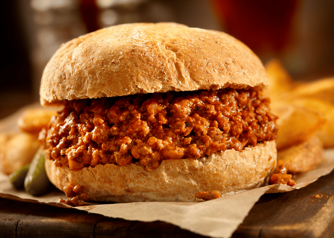 Sloppy Joe served on bun, on a plate with fries and a small pickle.