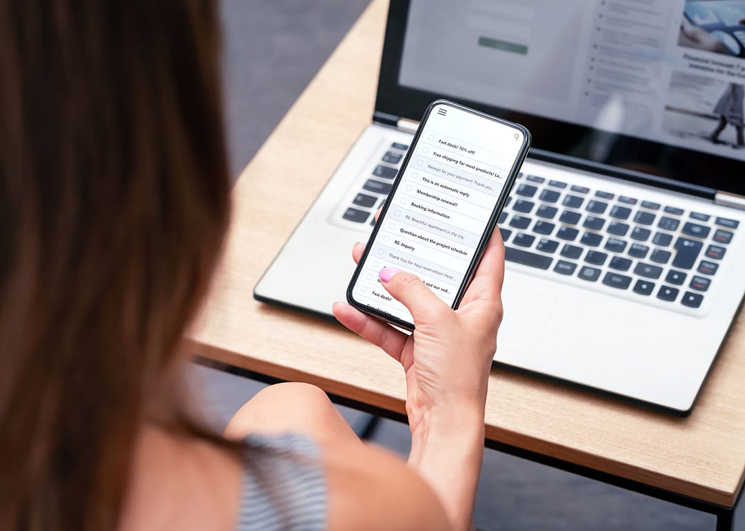 Person looking at email on phone with laptop open.