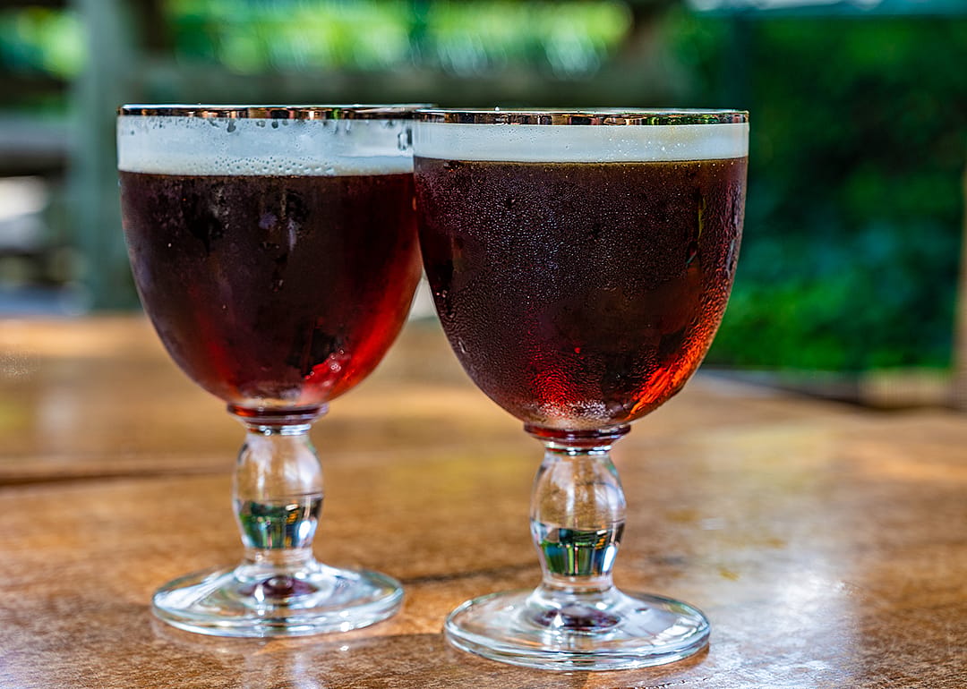 Two glasses of dark Belgian beer on table.