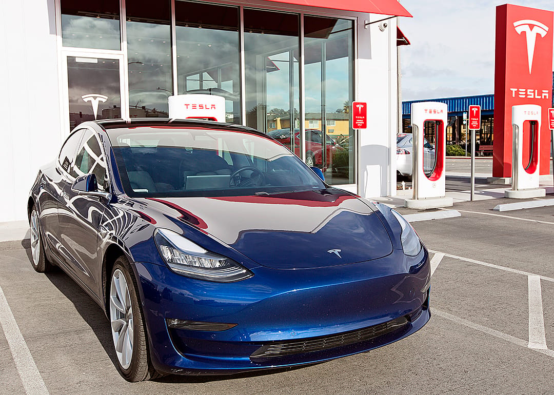 Navy Tesla Model 3 charging at supercharger station.