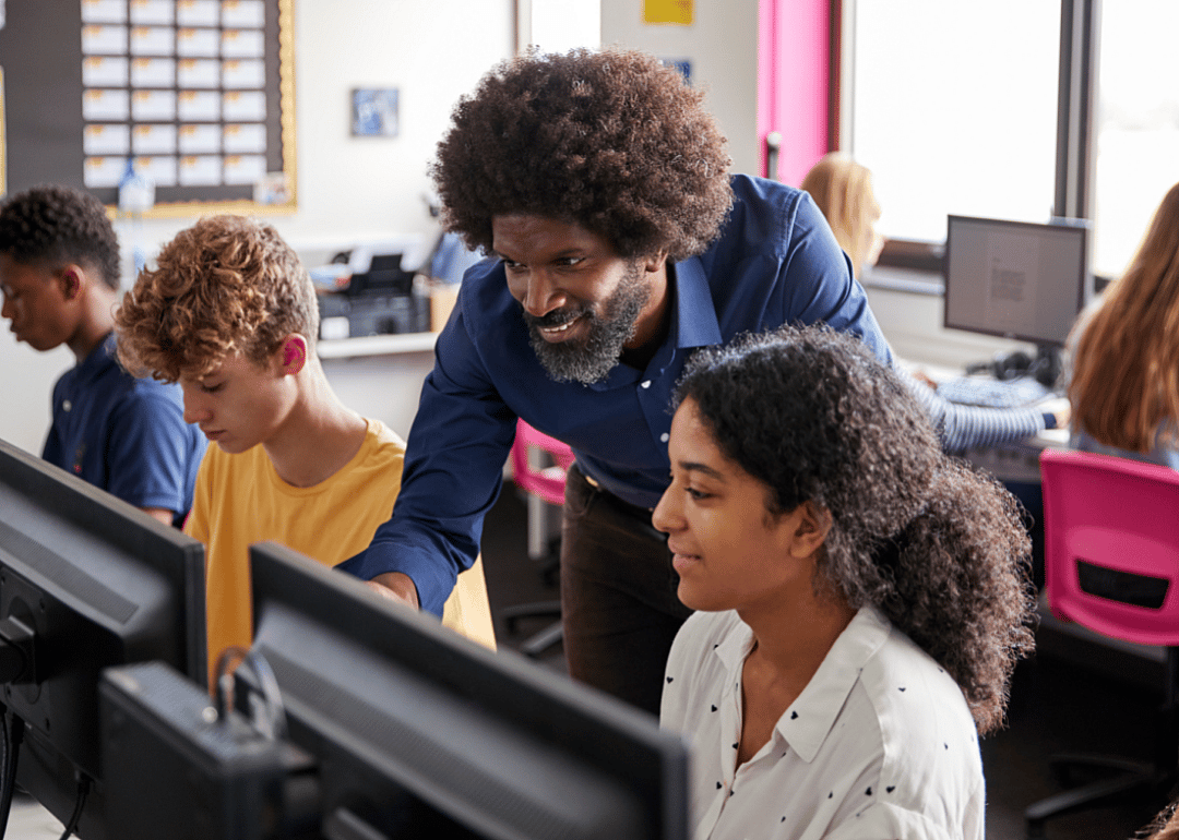 A teacher instructs a female student looking at a computer monitor