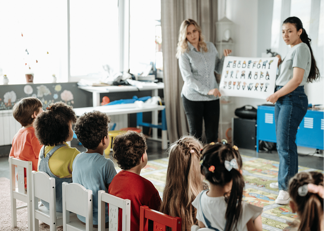 Two teachers hold up reading cards to a class of children