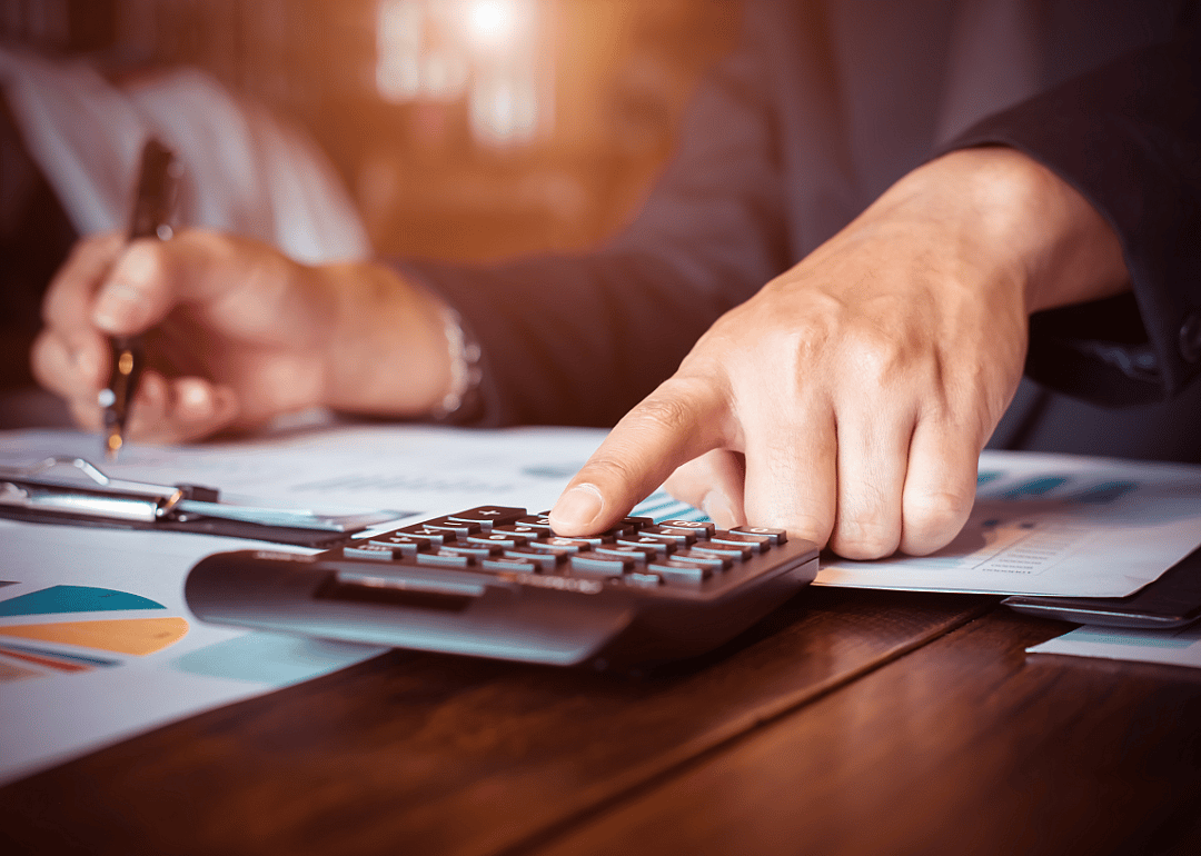 A man's hand calculates figures while reviewing documents