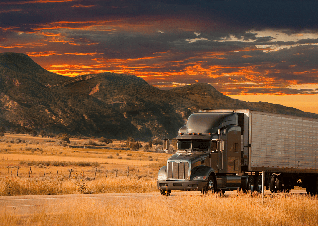A semi truck passes in front of a mountain range at sunset