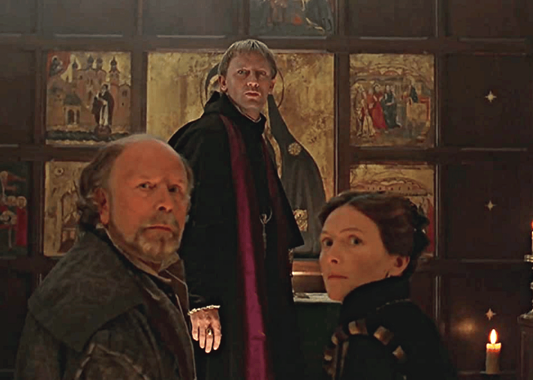 Daniel Craig stands behind a man and a woman seated looking surprised.