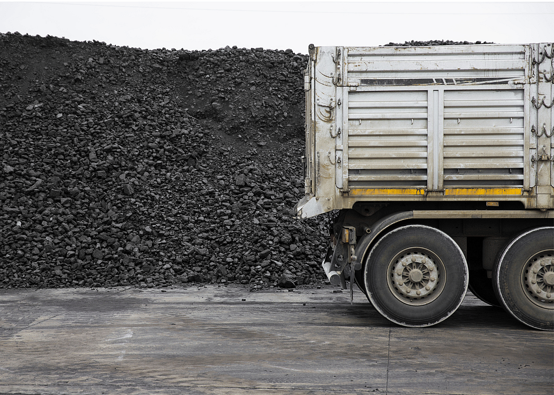 The rear trailer of a truck sits in front of a big pile of coal at a mining site.