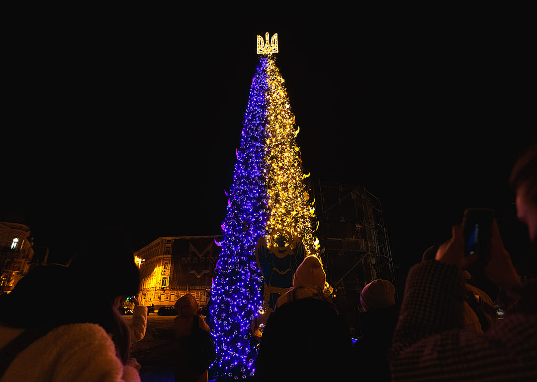 People visit a blue and gold Christmas tree lit by generators in Sofiivska Square, Kyiv.