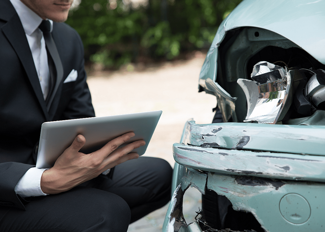 Insurance agent takes notes as he looks at damaged car.