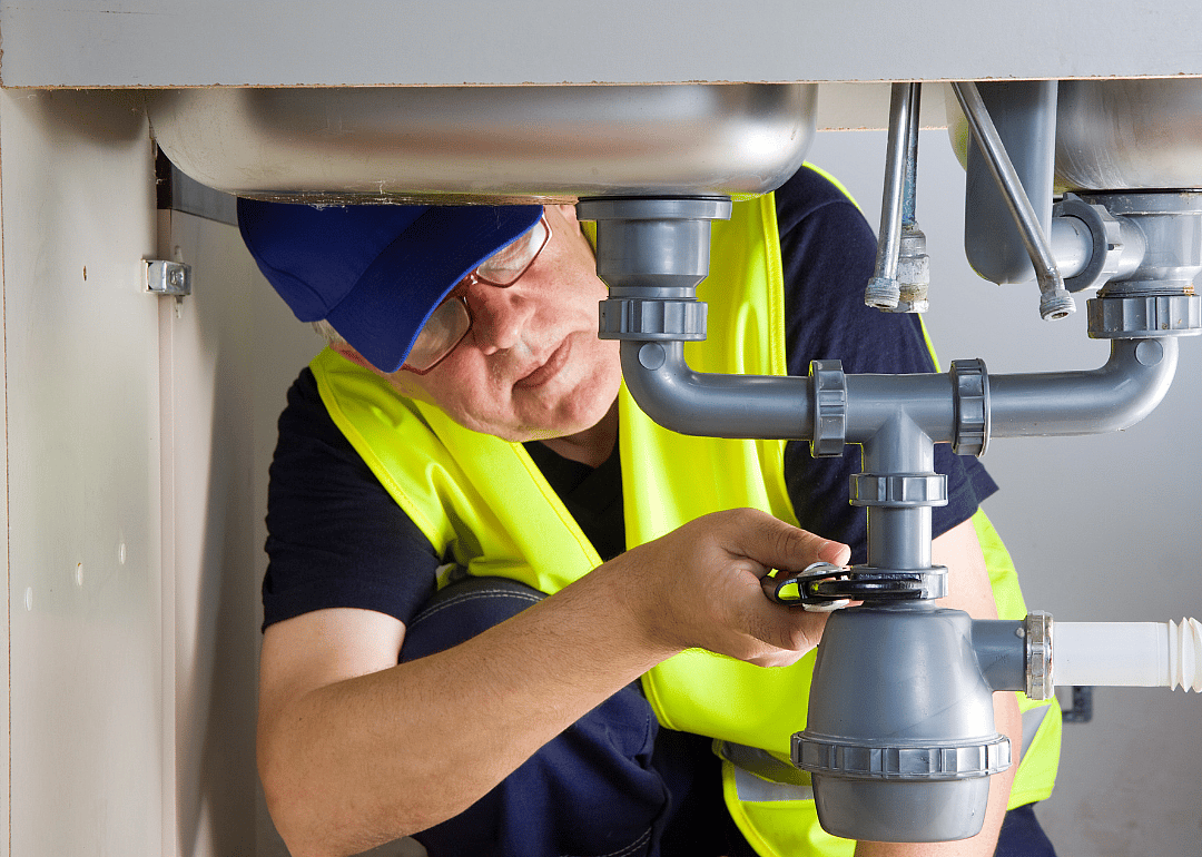 A plumber tightens a pipe under a sink.