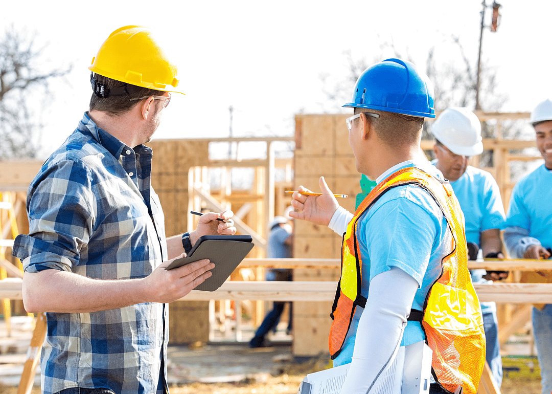 Construction workers wearing hard hats talk at a job site.