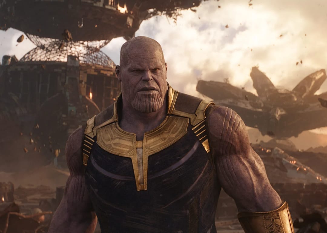 Josh Brolin dressed in armor with flying ships in a battle behind him.
