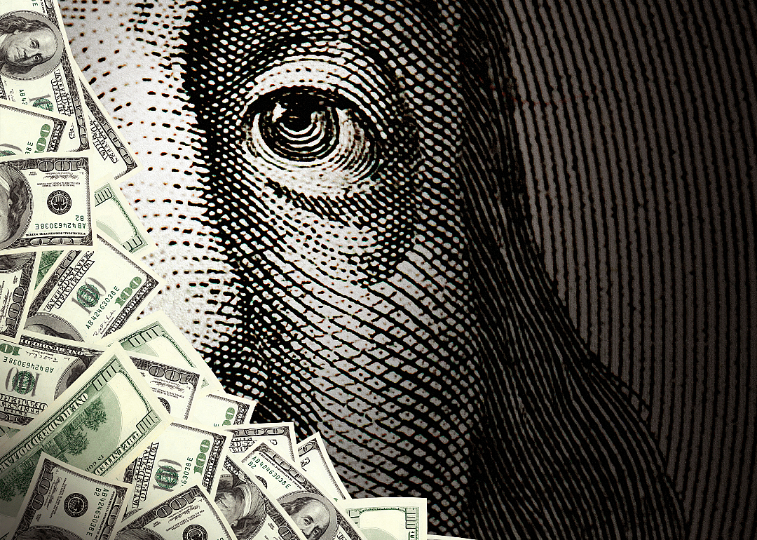 A pile of money sits a top a close up view of Benjamin Franklin as seen on a $100 bill.
