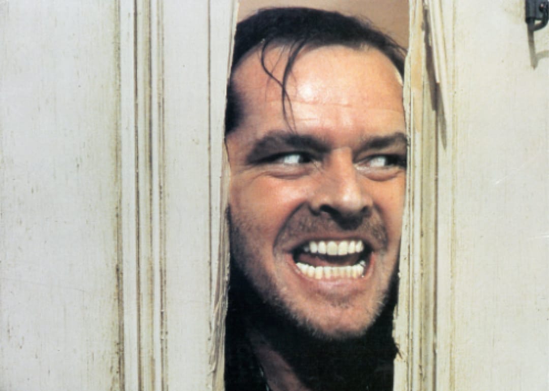 Jack Nicholson looking through two pieces of wood with a crazy look in his eyes.