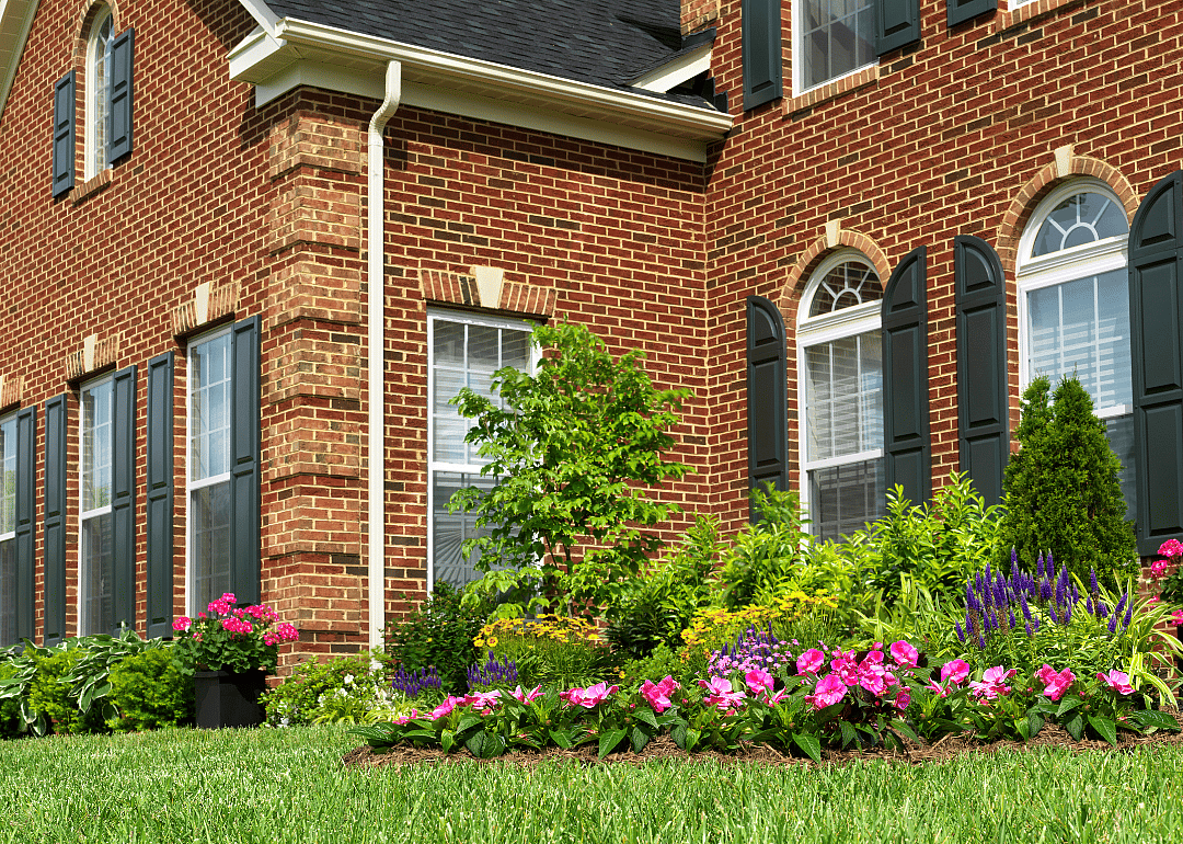 Exterior of a brick facade home with landscaping including a flower bed and lawn.