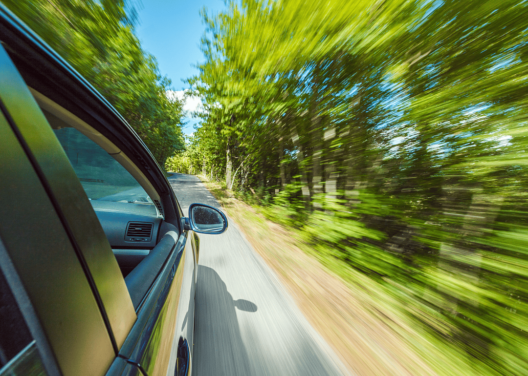A car speeding along a country road in the summer.