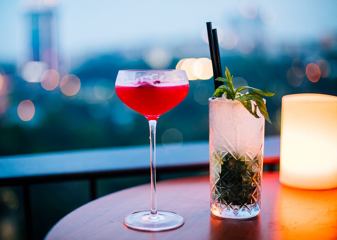 Two cocktails next to a candle on a rooftop bar table in the evening.