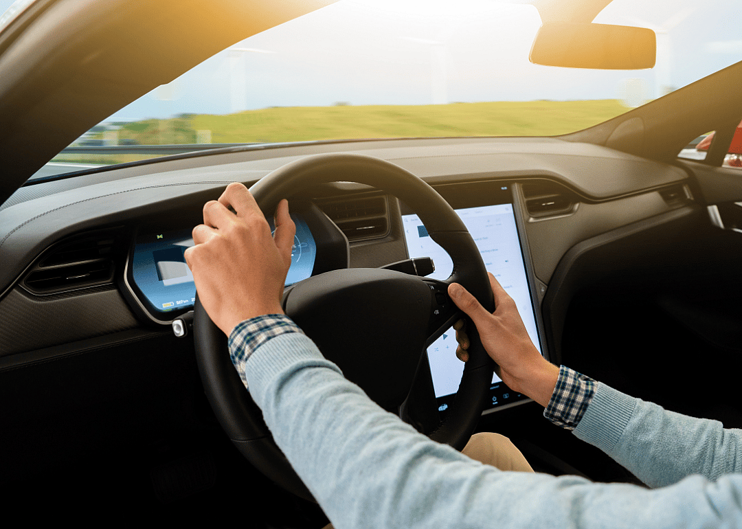 Person behind the wheel of an electric car driving down the road in the sunlight.