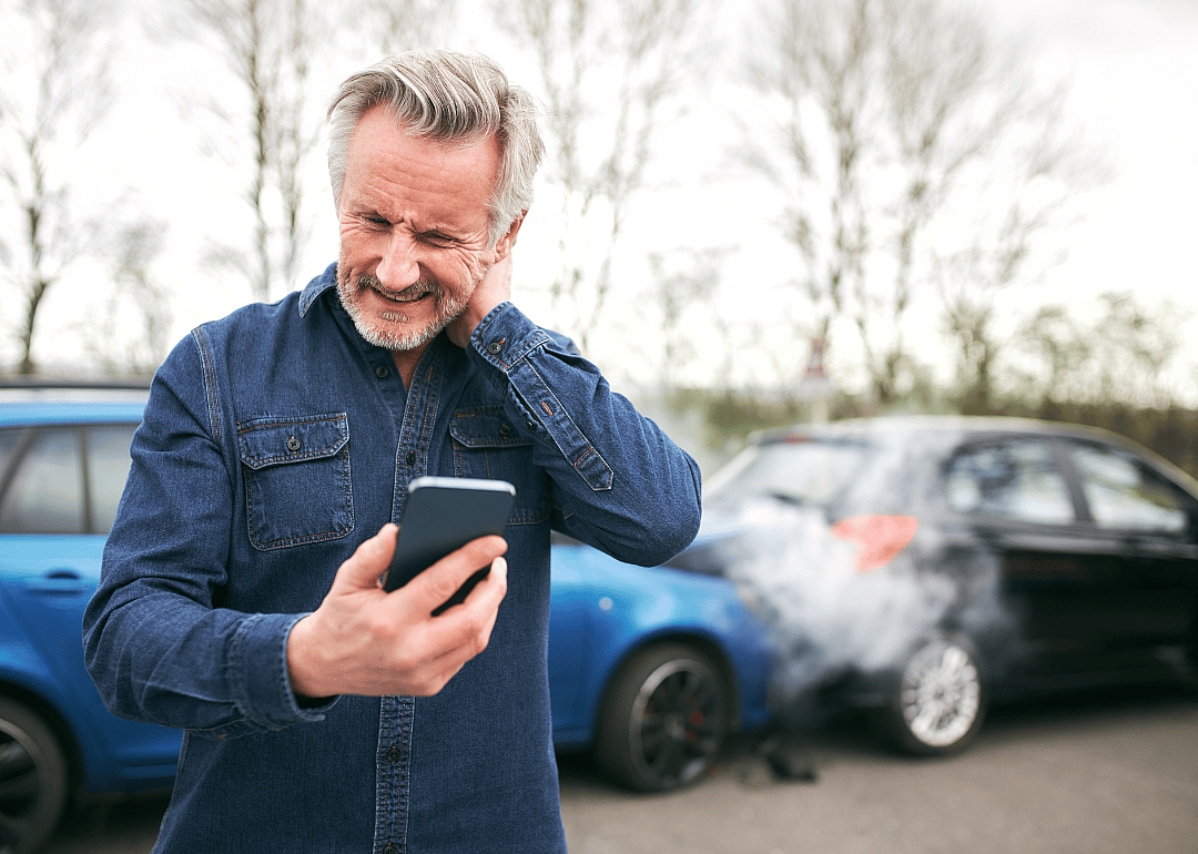 A man holds his neck in pain while making a phone call after an auto accident