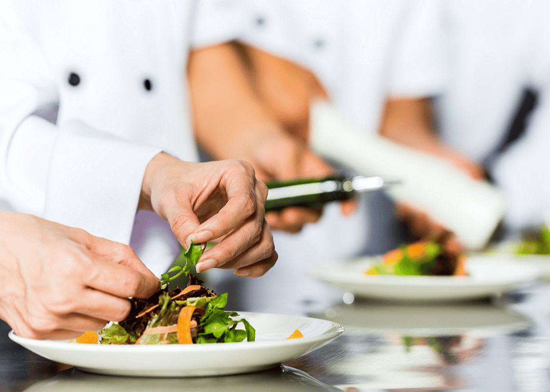 Two chefs preparing salads in a restaurant kitchen.