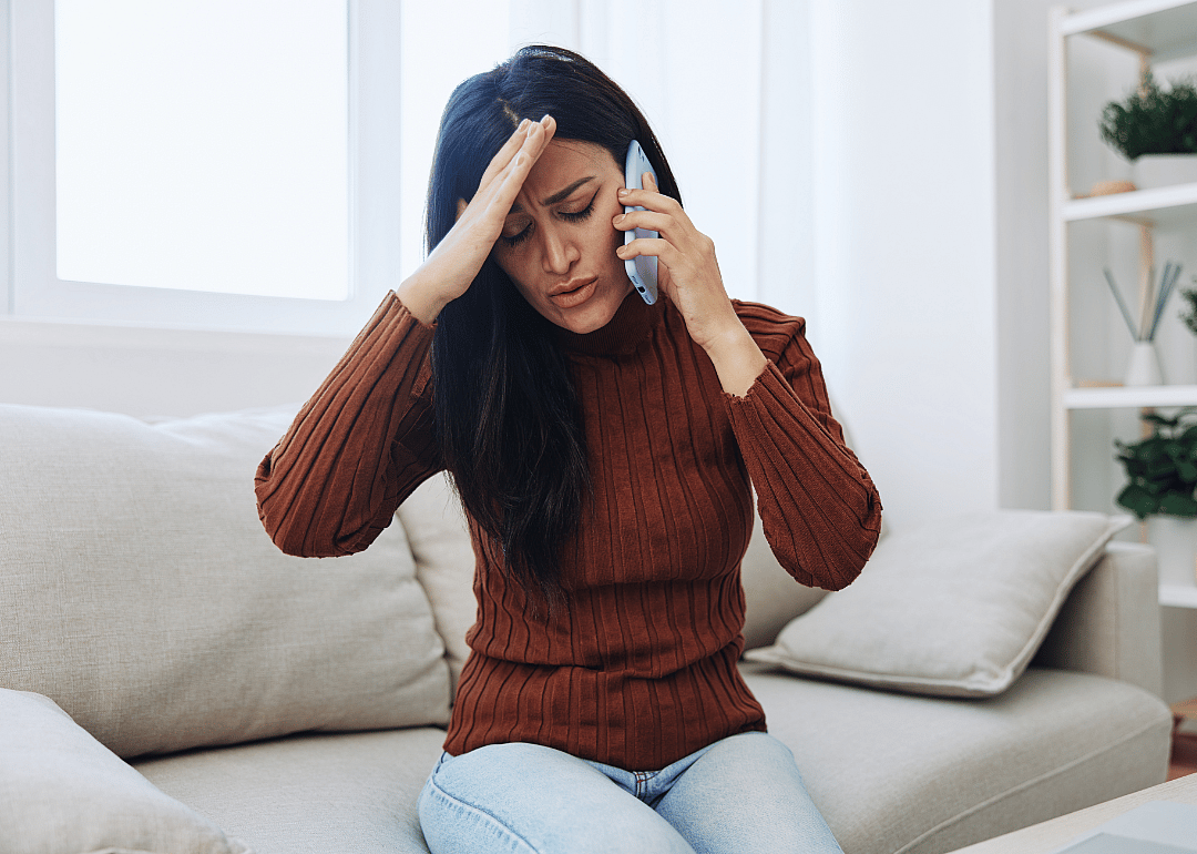 Frustrated woman sits on couch talking on the phone.