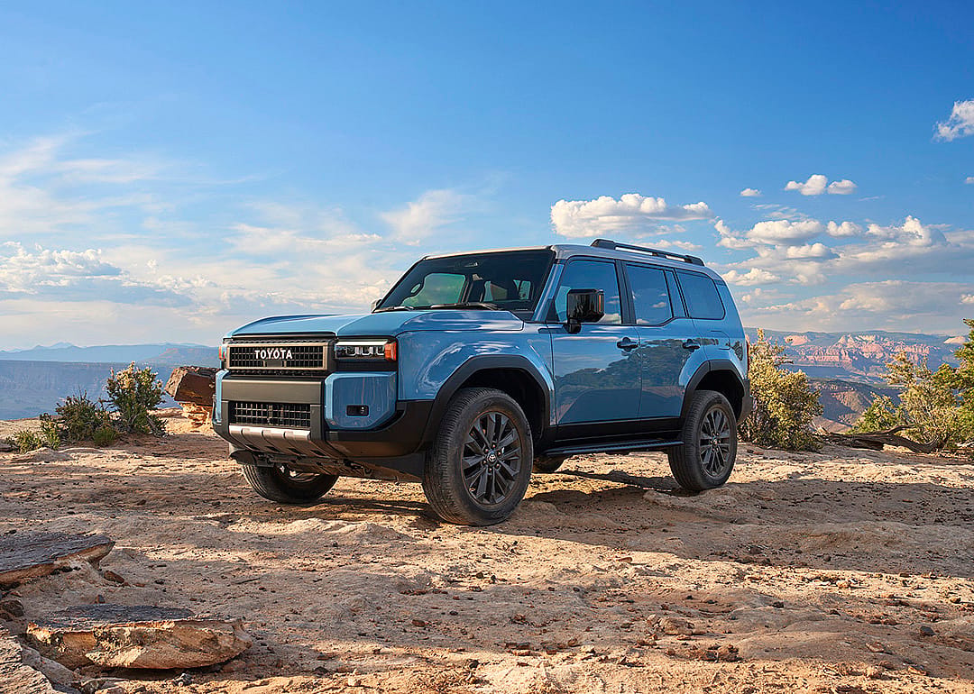 Blue Toyota Land Cruiser parked on rocky dir with sky in background.