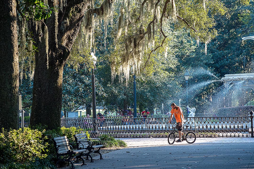 Forsyth Park fountain in Savannah, GA in October with a man in an orange shirt walking his BMX bike.