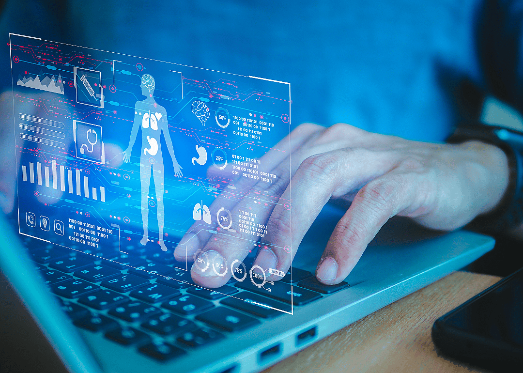 Hands typing on a laptop with an overlay of a virtual health care profile floating above the keyboard.