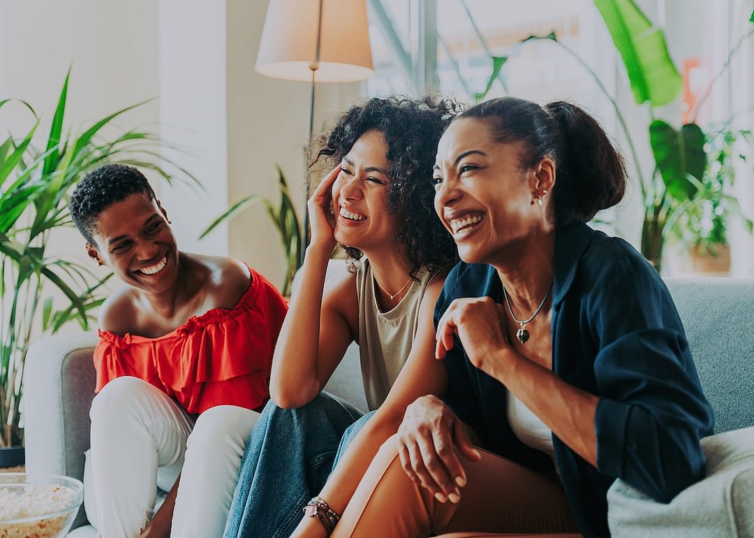 A group of three women hanging out and sitting on a couch together.