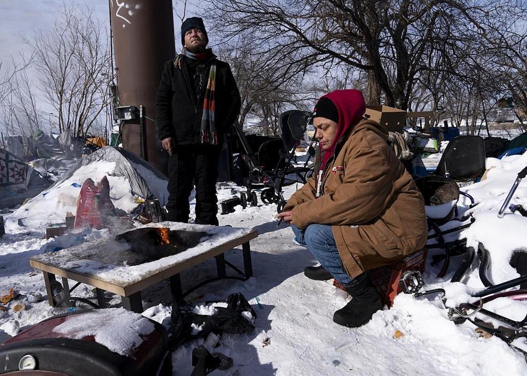 Two unhoused individuals sit around a fire in the homeless camp in Oklahoma City, Oklahoma.